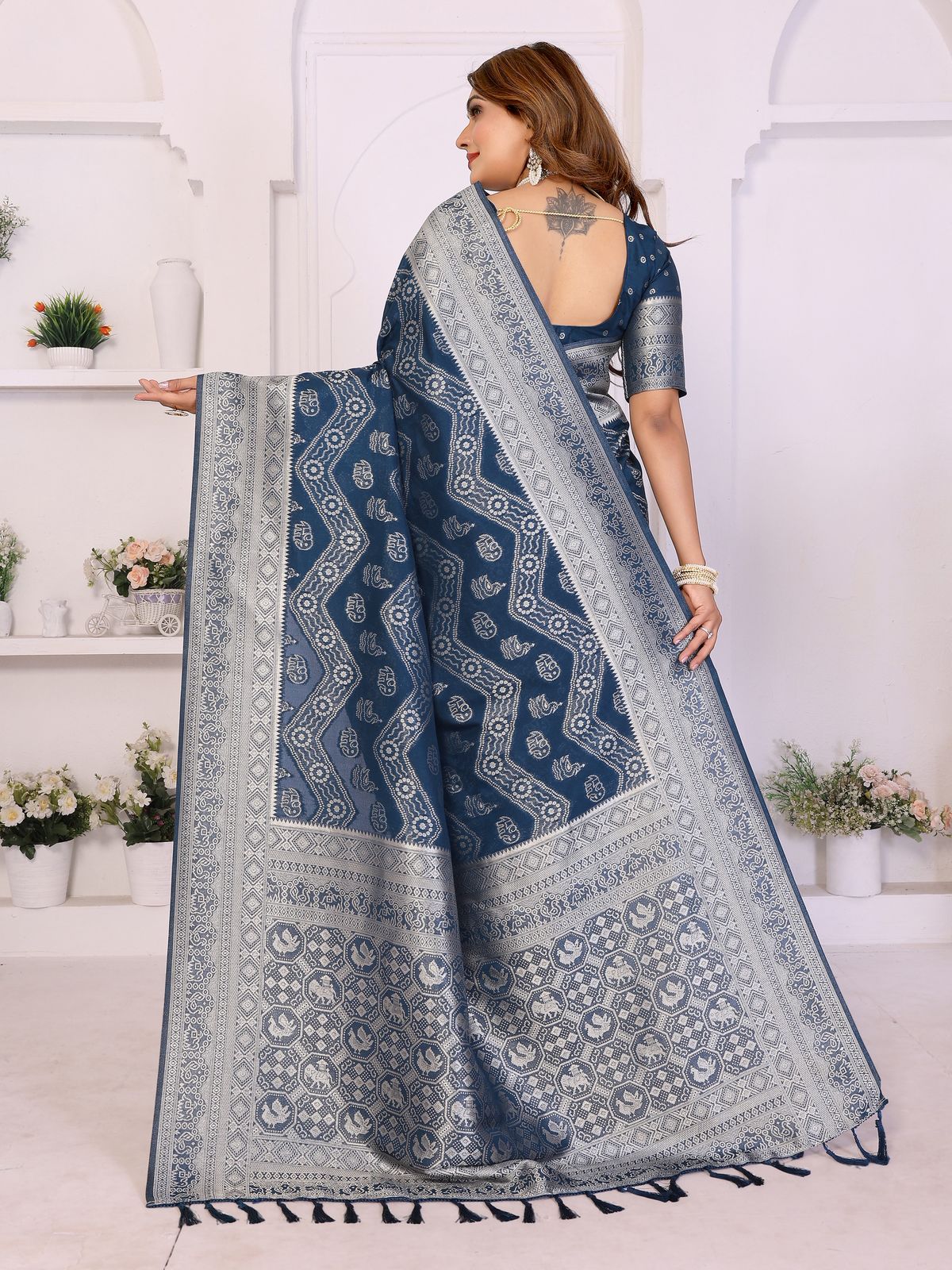 Woman wearing a blue saree with a white pattern in a bright room.