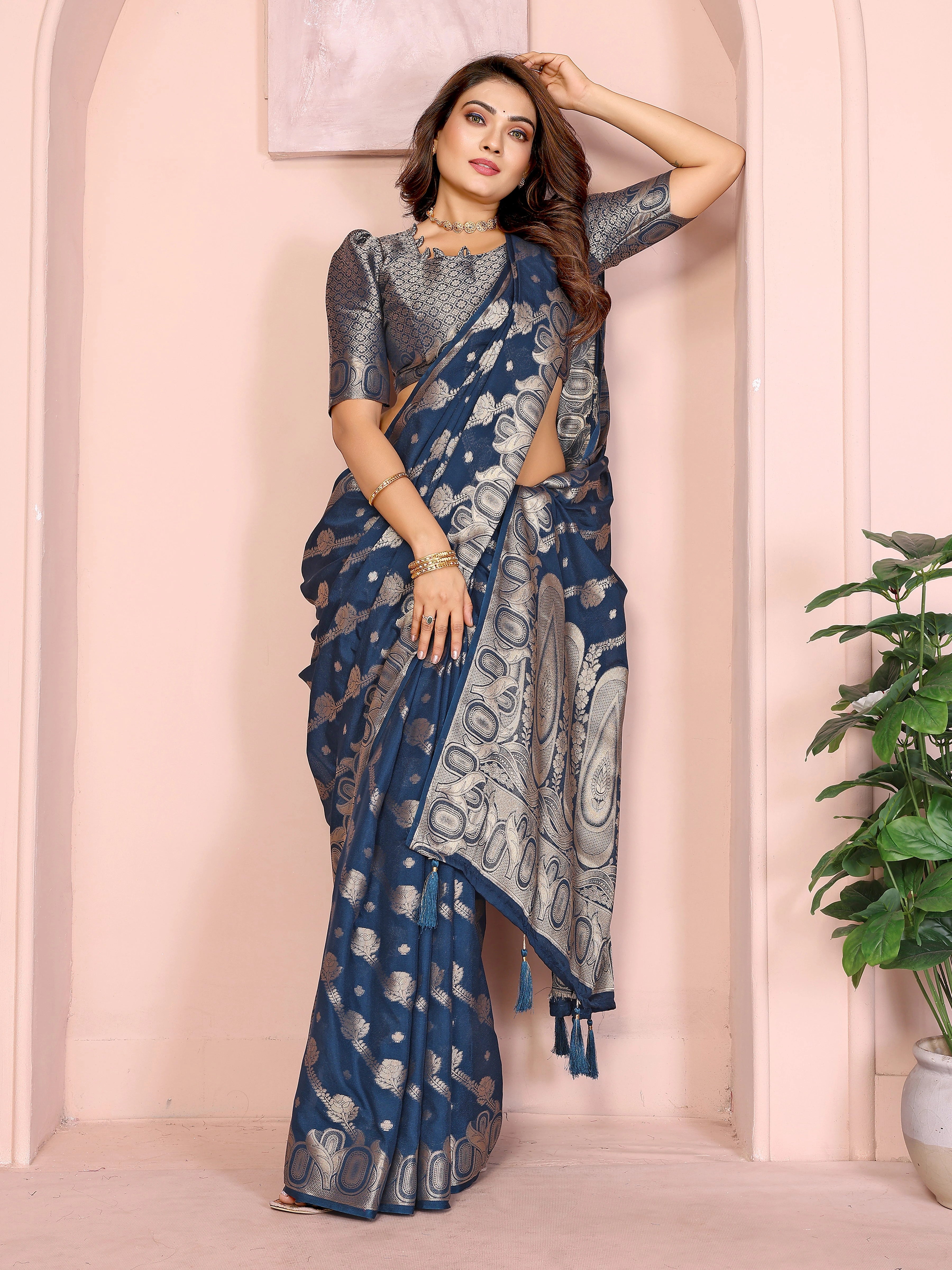 Woman wearing a blue saree with a white pattern against a pink wall.