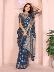 Woman wearing a blue saree with a white pattern against a pink wall.