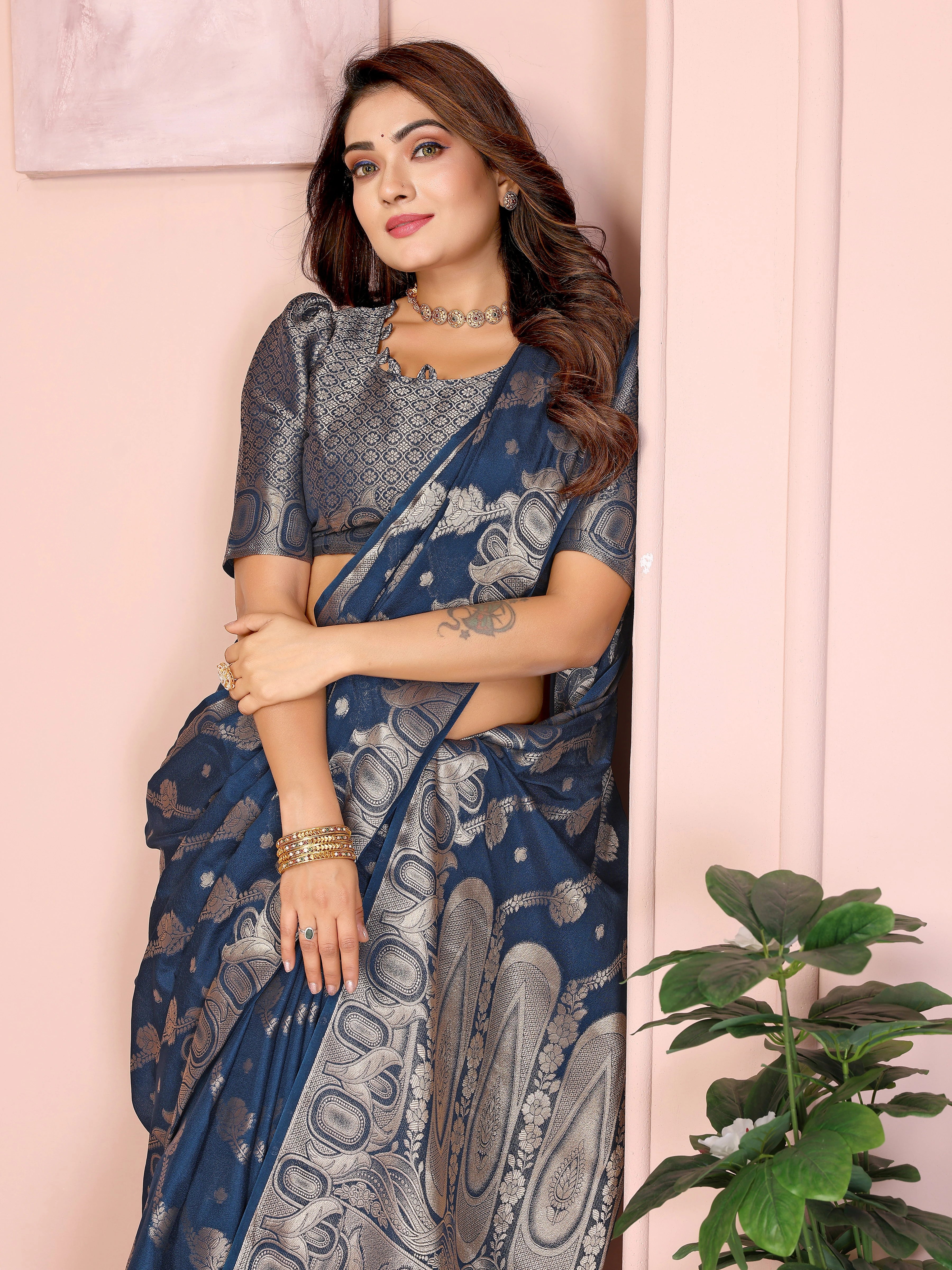 Woman wearing a blue saree with a white pattern against a light pink wall.