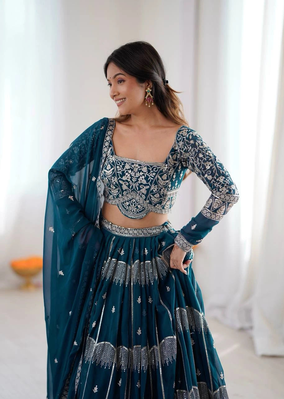 Woman wearing a traditional teal and silver embroidered outfit with a sheer dupatta.