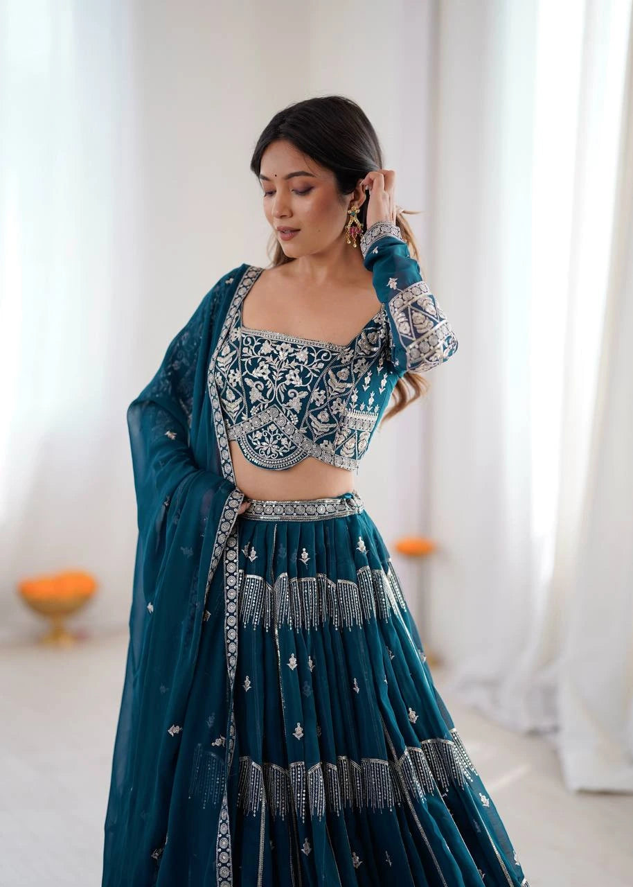 Woman in a teal embroidered traditional outfit with a white background
