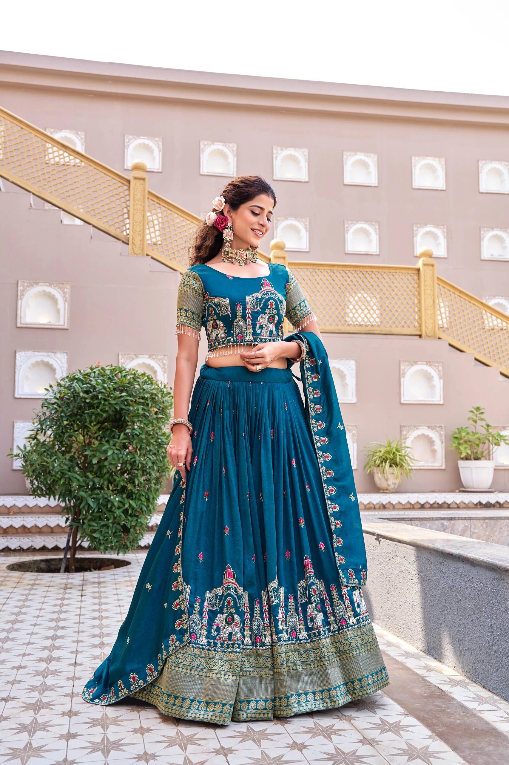 Woman in a traditional teal and green outfit standing in front of a decorative building.