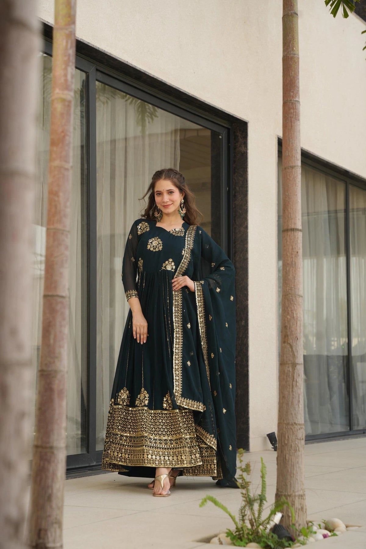 Woman in a dark blue traditional outfit with gold details standing in front of a building.