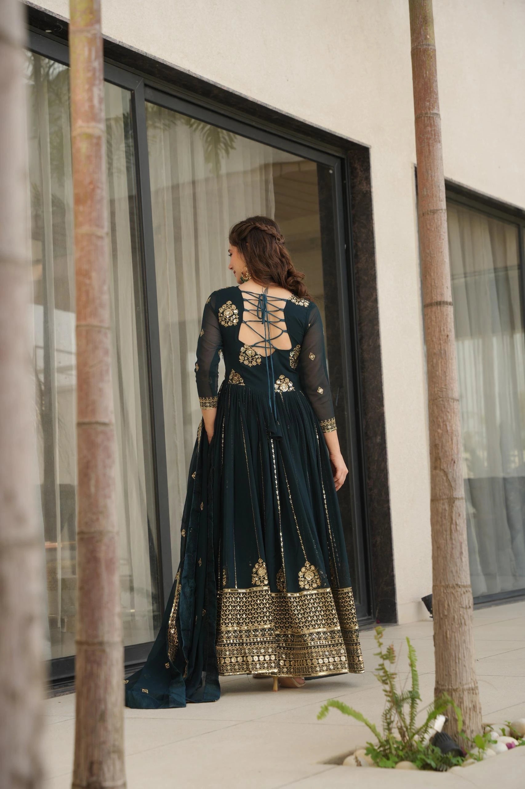 Woman in a dark green and gold traditional outfit standing in front of a modern building.