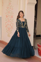 Woman in a dark blue gown with floral embroidery standing indoors.