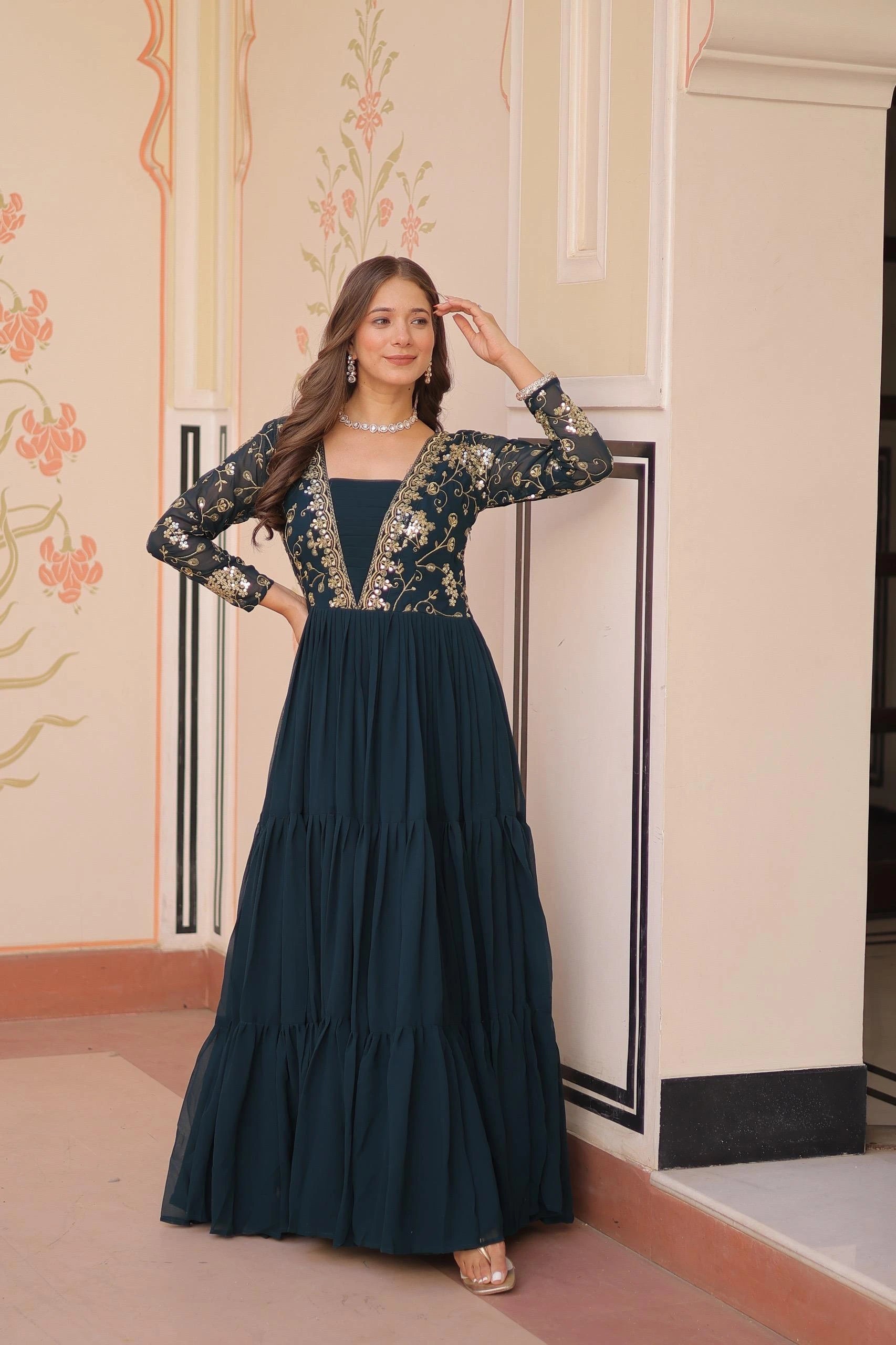Woman wearing a dark blue dress with floral embroidery in an elegant interior setting.