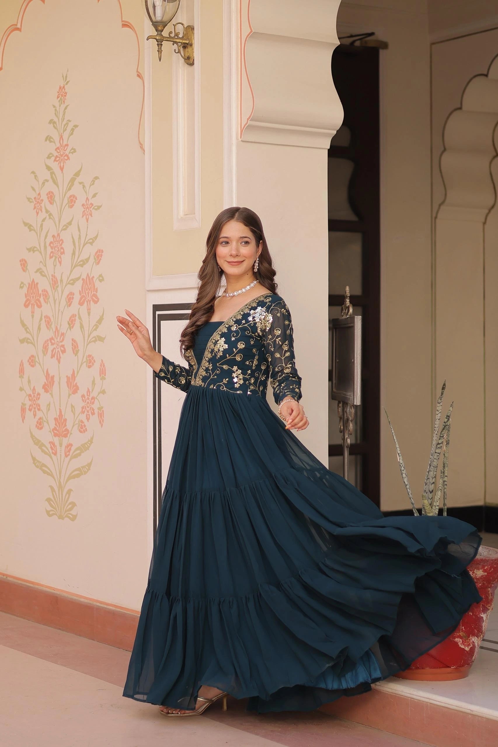 Woman in a long, dark blue embroidered dress standing in a decorated room.