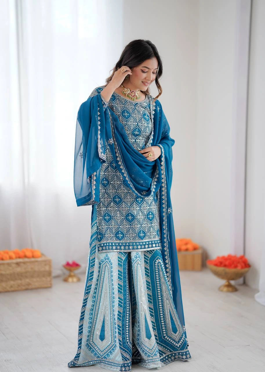 Woman in a blue and white embroidered traditional outfit with a matching shawl, standing against a white background.
