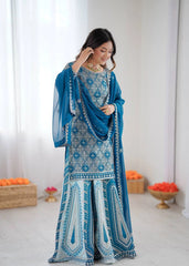 Woman in a blue and white embroidered traditional outfit with a matching shawl, standing against a white background.