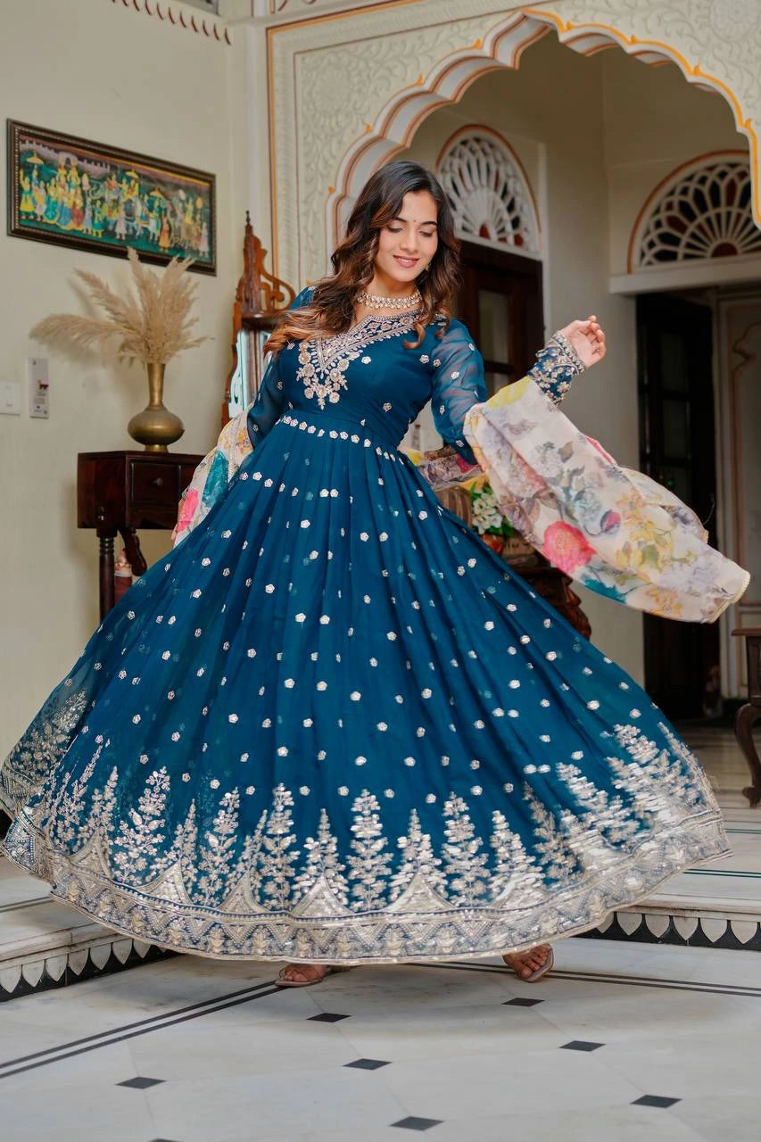 Woman in a blue embroidered dress posing in a decorated room.