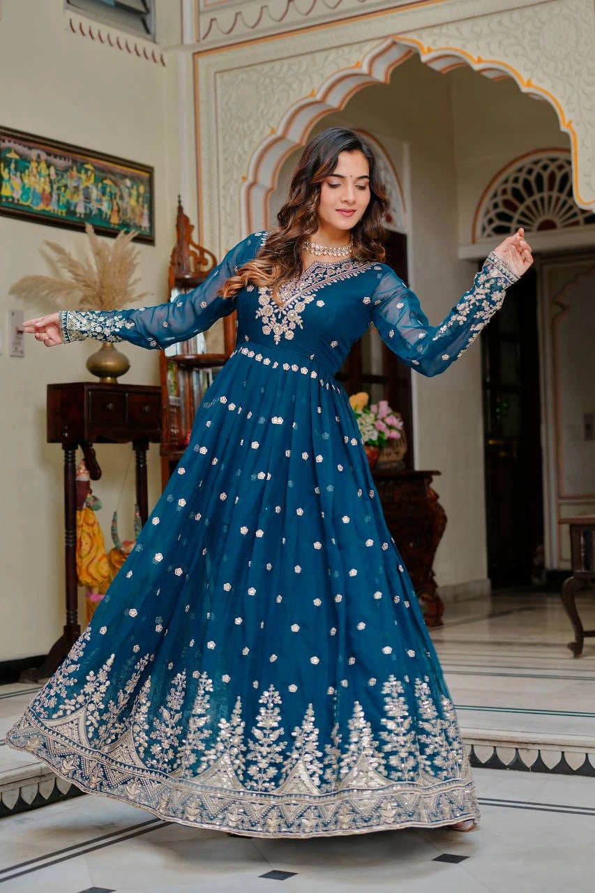 Woman in a blue embroidered dress posing in an ornate room.