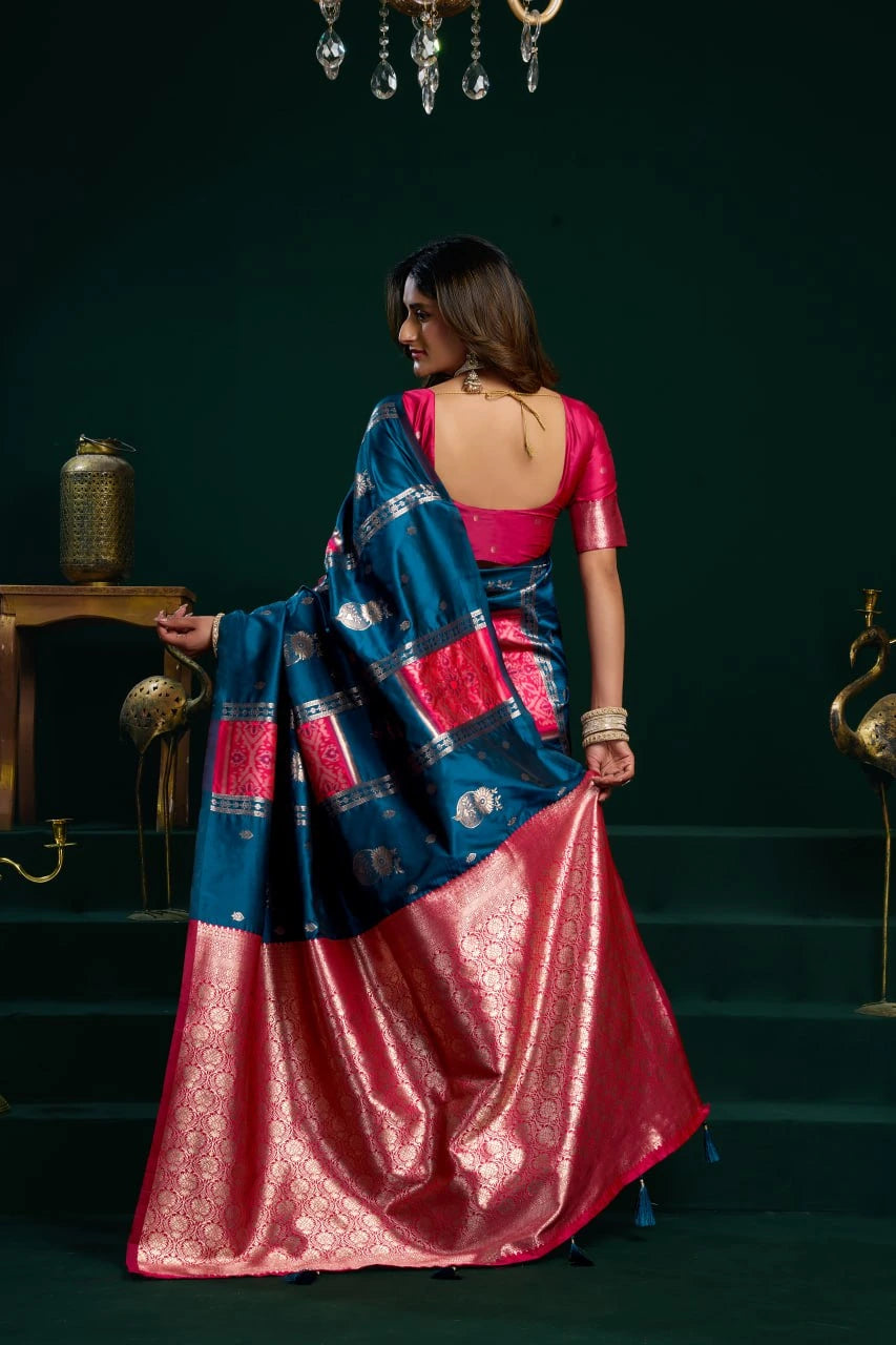 Woman in a blue and pink saree standing against a dark green background