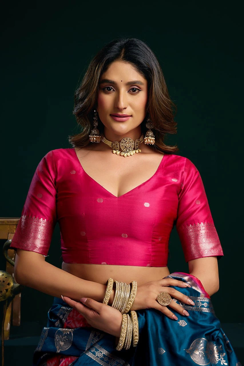 Woman wearing a pink blouse and blue saree with jewelry against a dark background