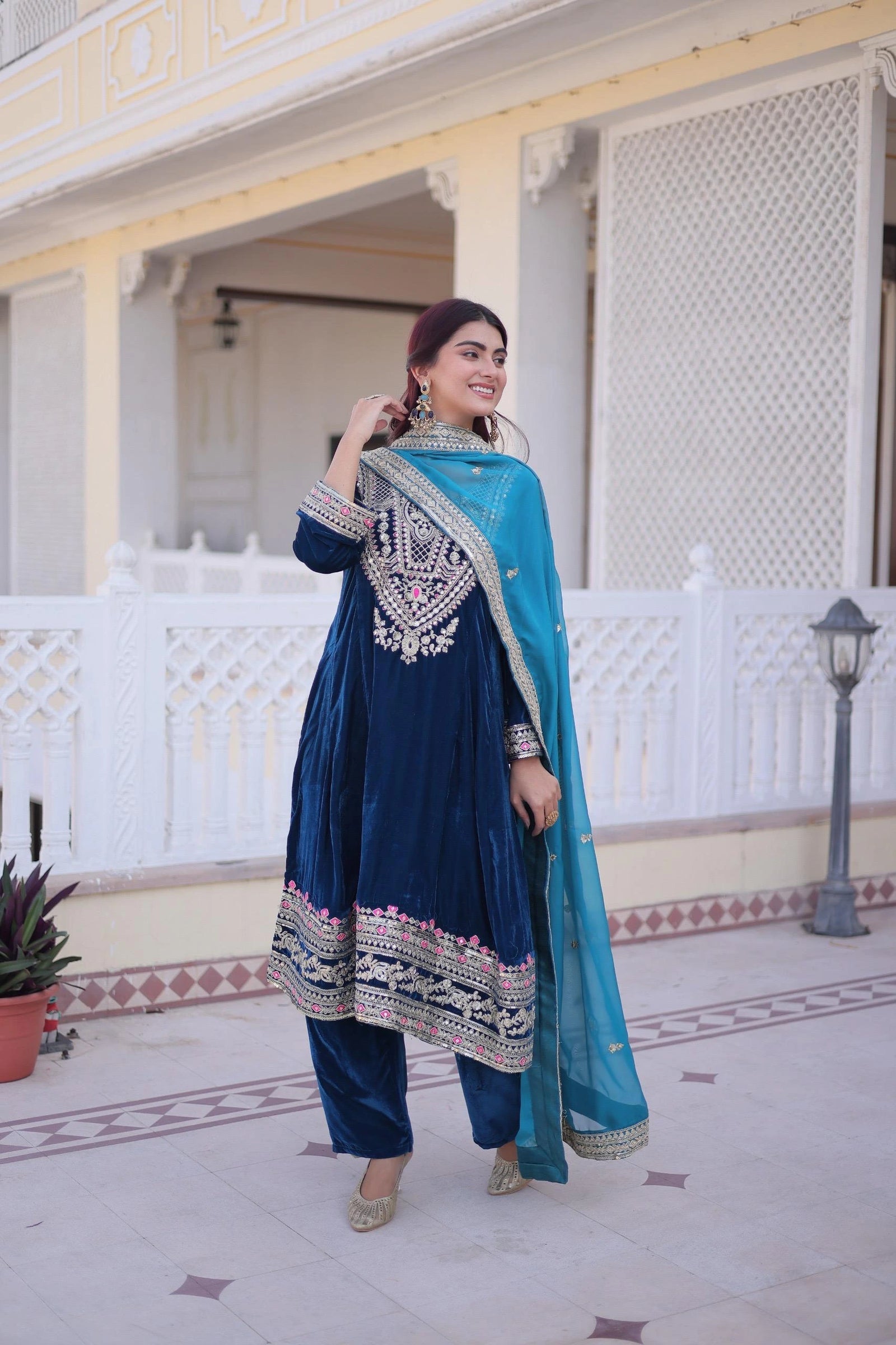 Woman in traditional blue and silver outfit standing in front of a decorative building.