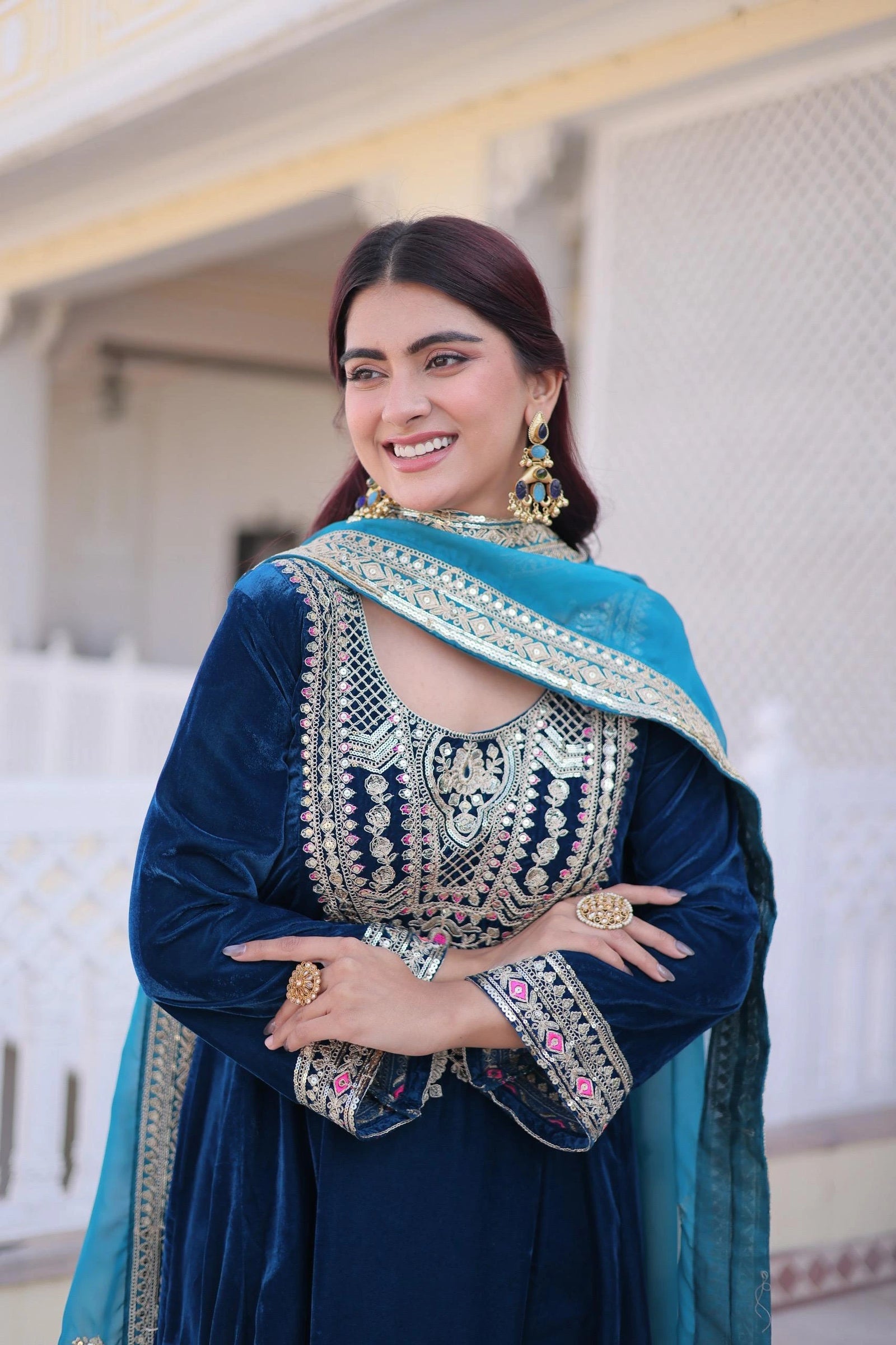 Woman in traditional blue and green outfit with intricate patterns, standing indoors.