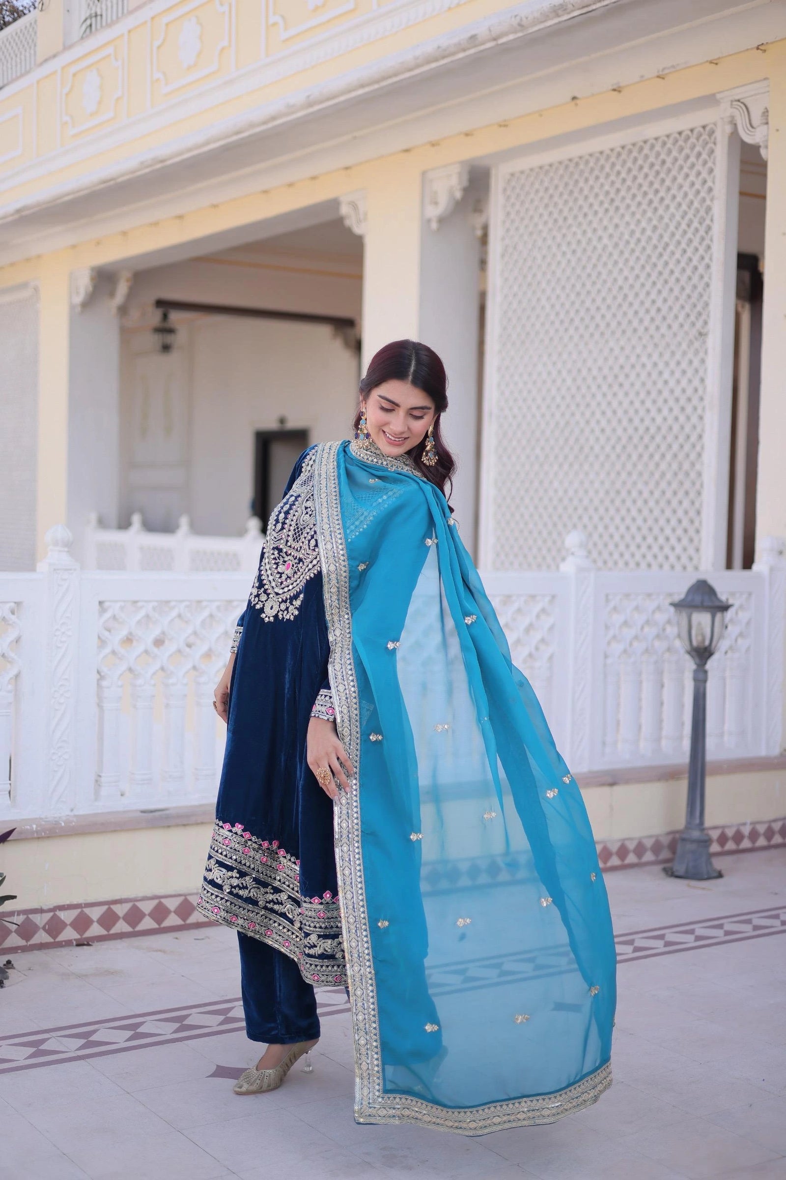 Woman in a blue traditional outfit standing in front of an architectural building.