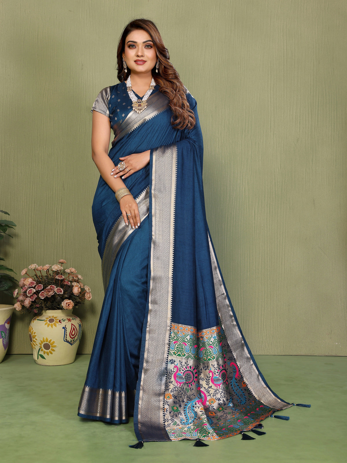 Woman wearing a blue saree with a floral border on a green background