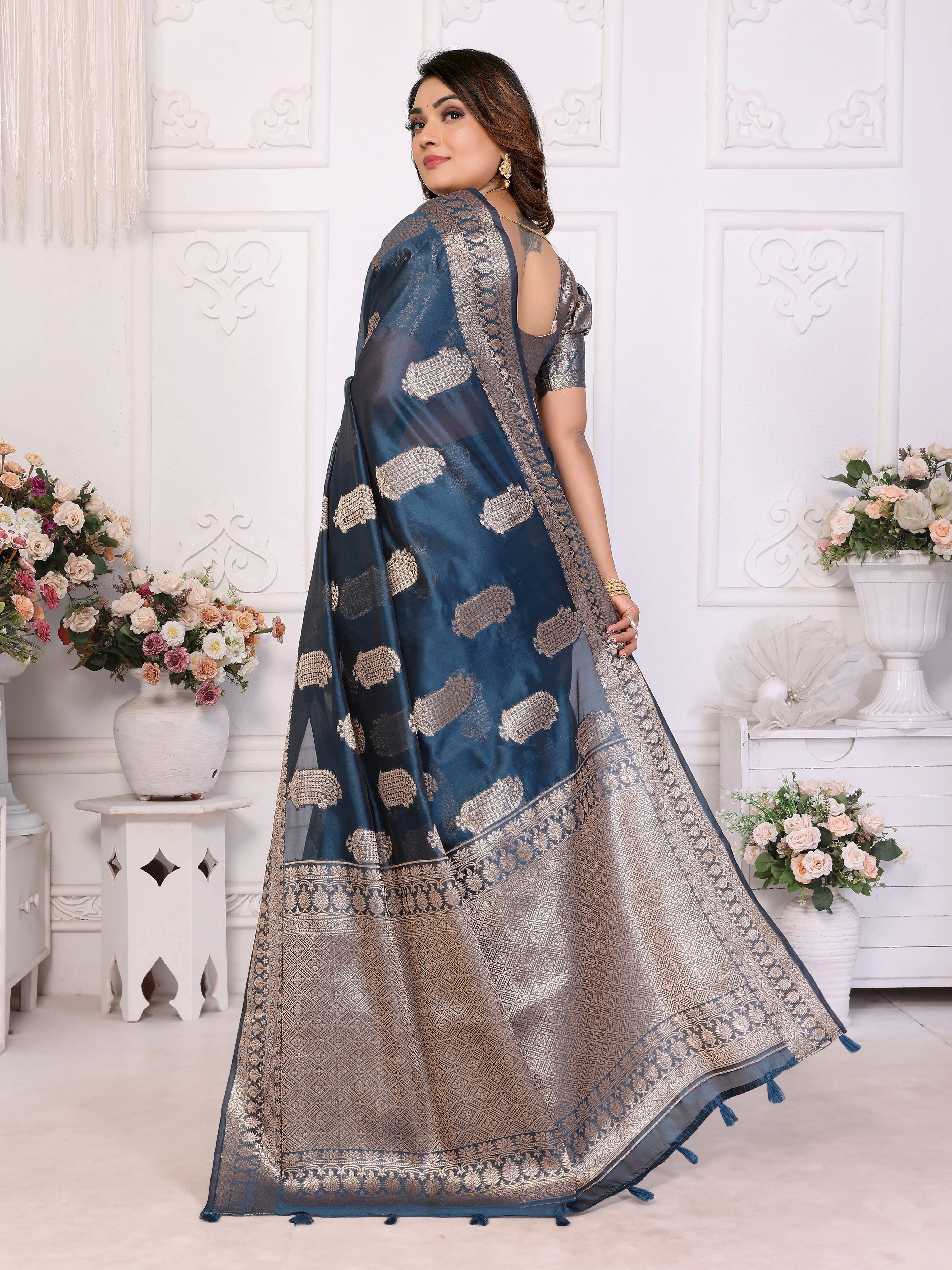 Woman wearing a blue and beige saree with floral decorations in the background