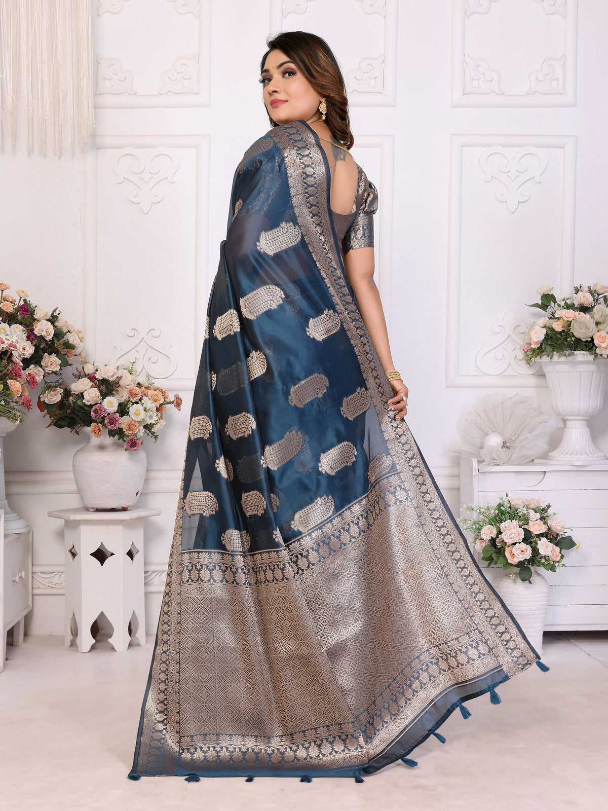 Woman wearing a blue and beige saree with floral decorations in the background