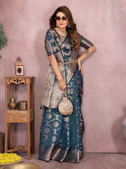 Woman in a traditional saree standing next to a wooden shelf with decorative items.
