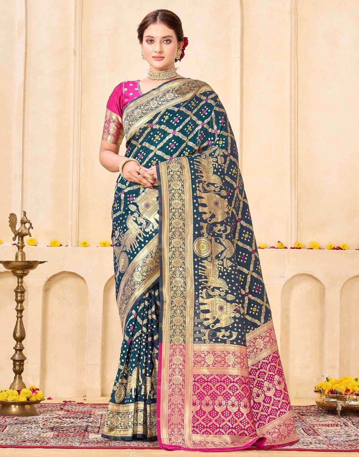Woman wearing a blue and pink saree with intricate patterns in a decorated indoor setting.