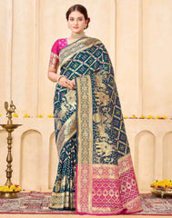 Woman wearing a blue and pink saree with intricate patterns in a decorated indoor setting.