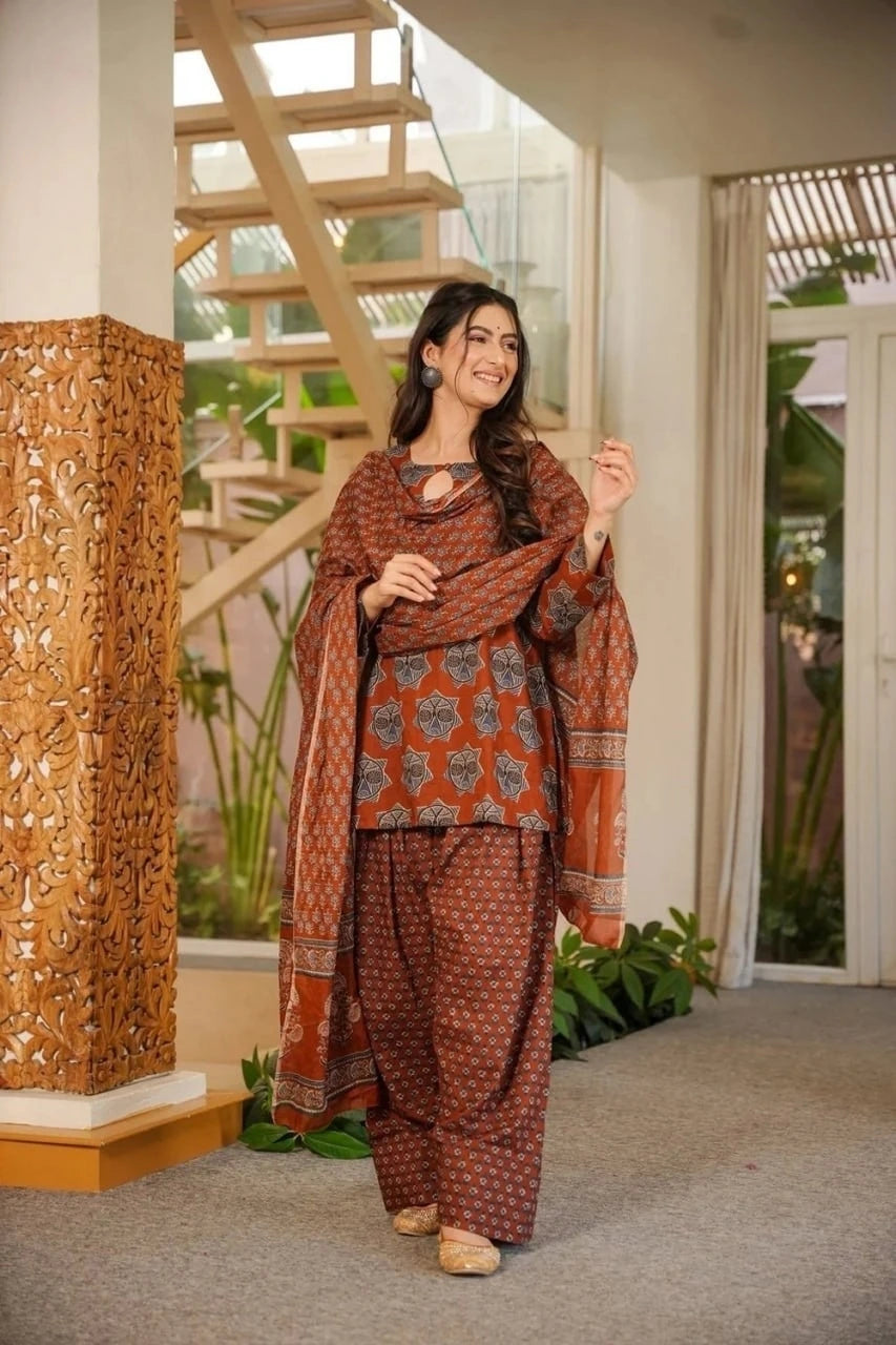 Woman in traditional patterned outfit standing indoors with decorative elements.
