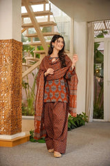 Woman in traditional patterned outfit standing indoors with decorative elements.