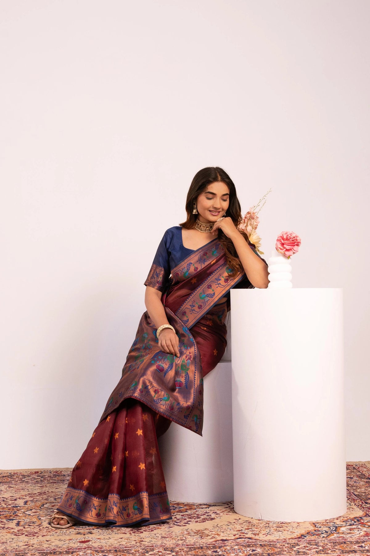 Woman in a traditional saree holding a flower against a white background