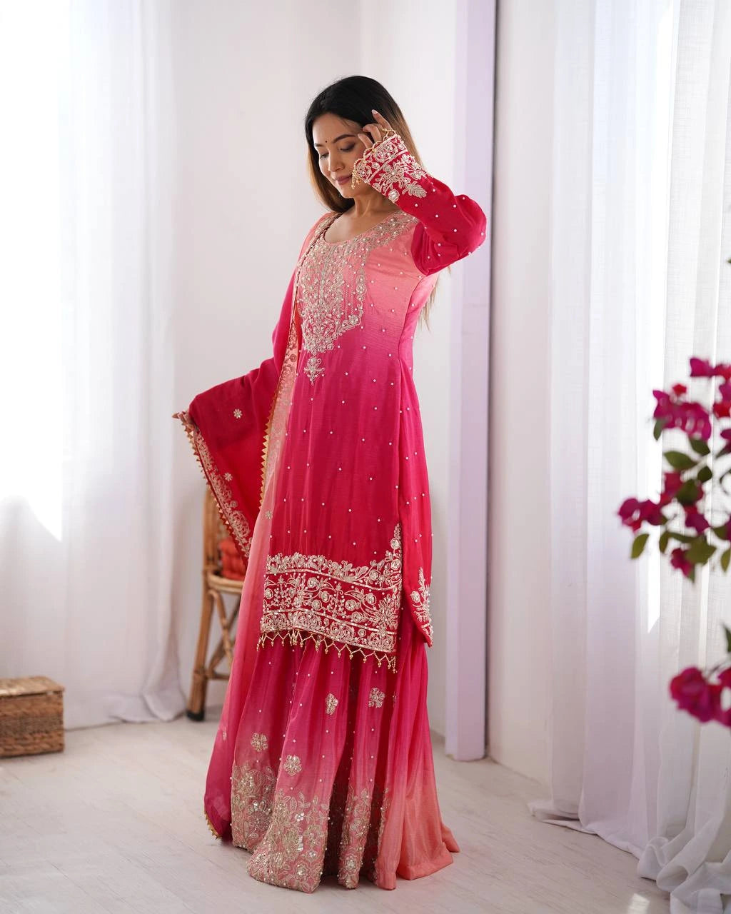 Woman in a pink traditional outfit with white embroidery standing in a bright room.