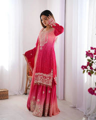 Woman in a pink traditional outfit with white embroidery standing in a bright room.