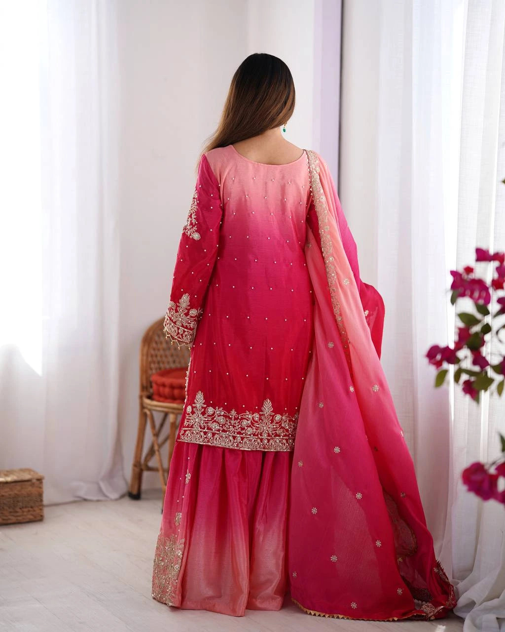 Woman wearing a pink traditional outfit with white curtains and flowers in the background