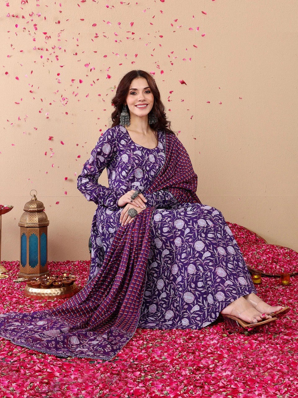 Woman in a purple traditional outfit sitting on a pink floral carpet with decorative elements.