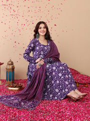 Woman in a purple traditional outfit sitting on a pink floral carpet with decorative elements.