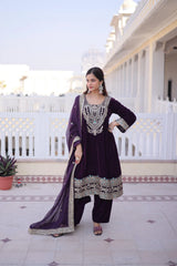 Woman in a purple traditional outfit standing on a patio with white railing and building in the background.
