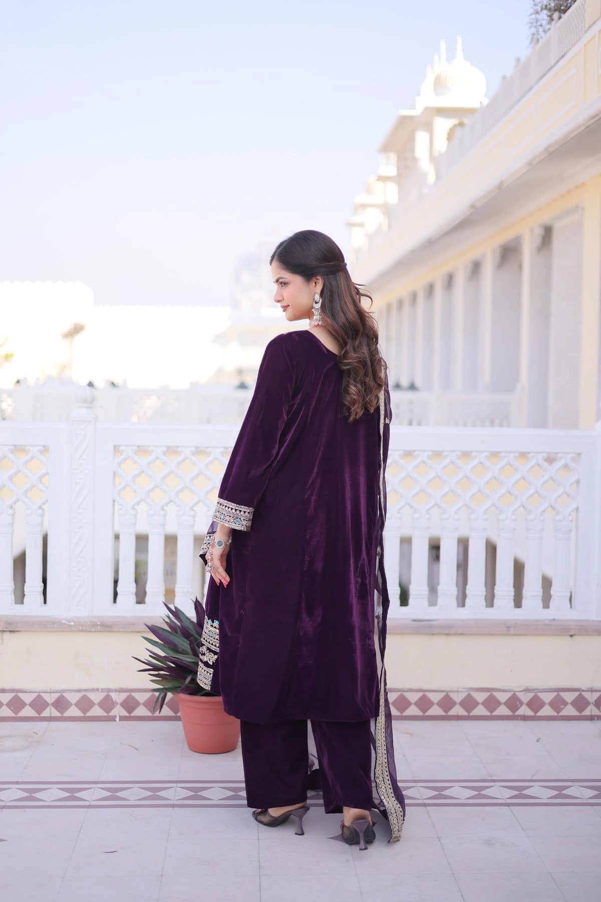 Woman in a purple traditional outfit standing on a rooftop with white architectural elements.