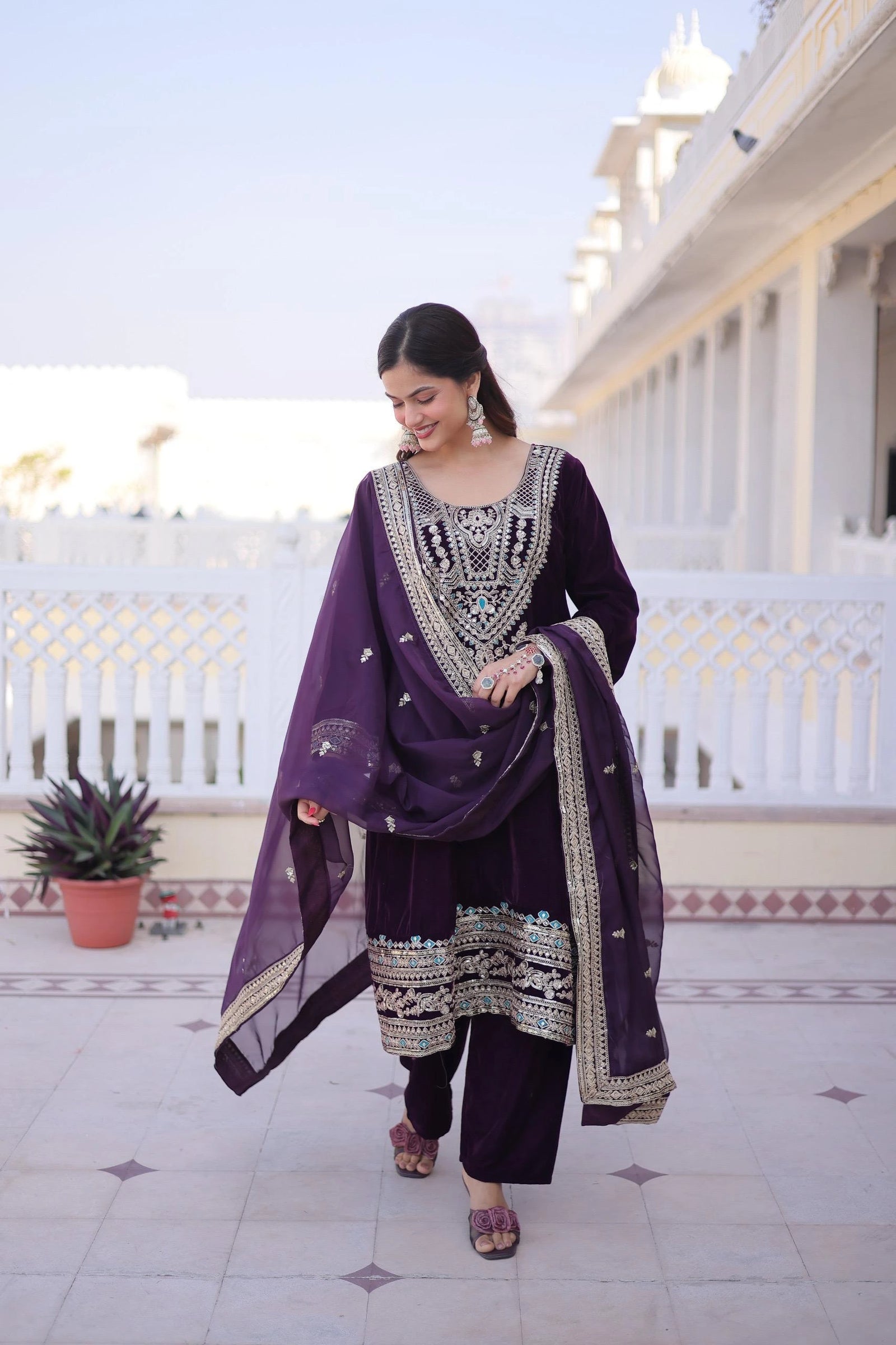 Woman in a purple traditional outfit standing on a balcony with a building and sky in the background