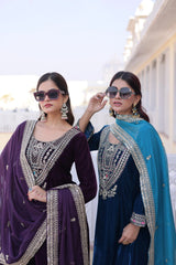 Two women wearing traditional embroidered sarees outdoors with a clear sky.