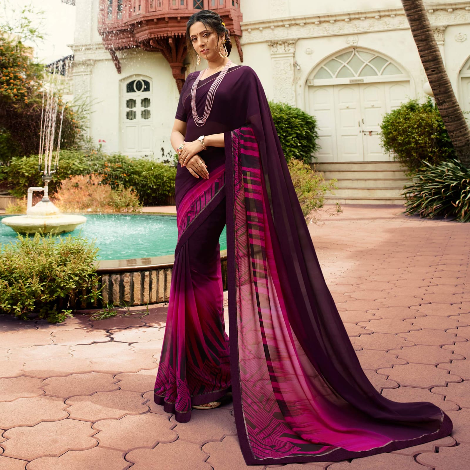 Woman in a deep shade purple jacquard work saree with gold border standing indoors in an elegant room with arched decor and vintage furniture elements