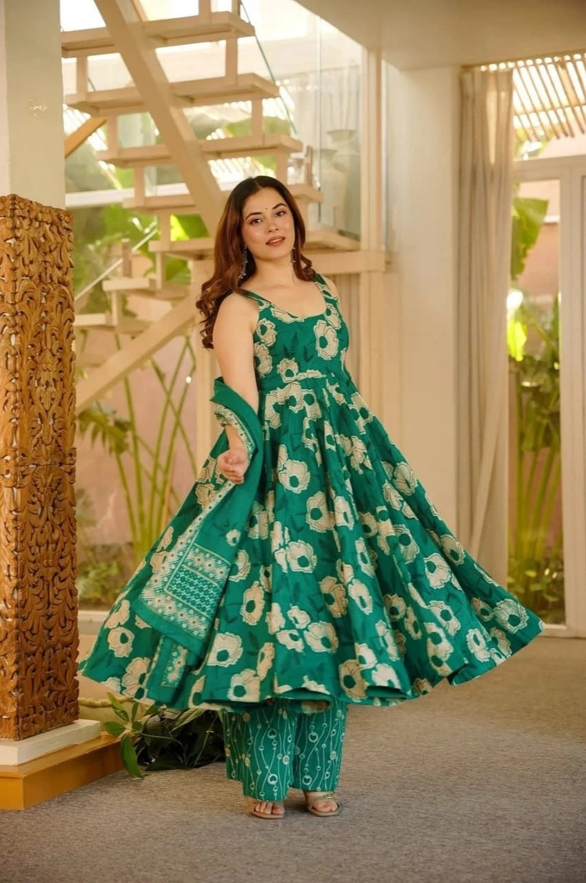 Woman in a green floral dress standing in a room with large windows.