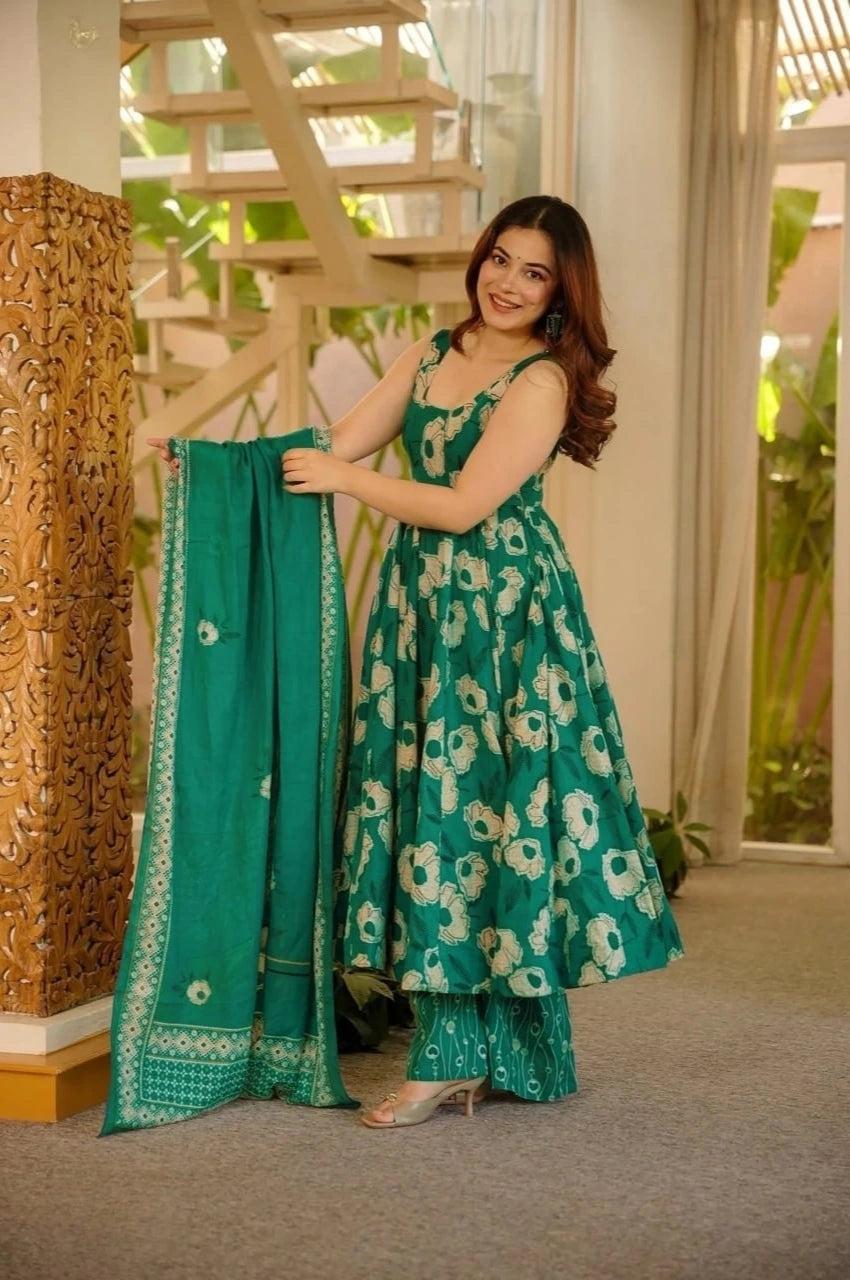 Woman in a green floral dress holding a matching dupatta indoors.