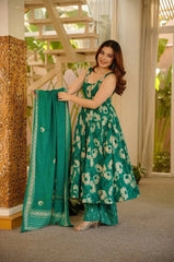 Woman in a green floral dress holding a matching dupatta indoors.