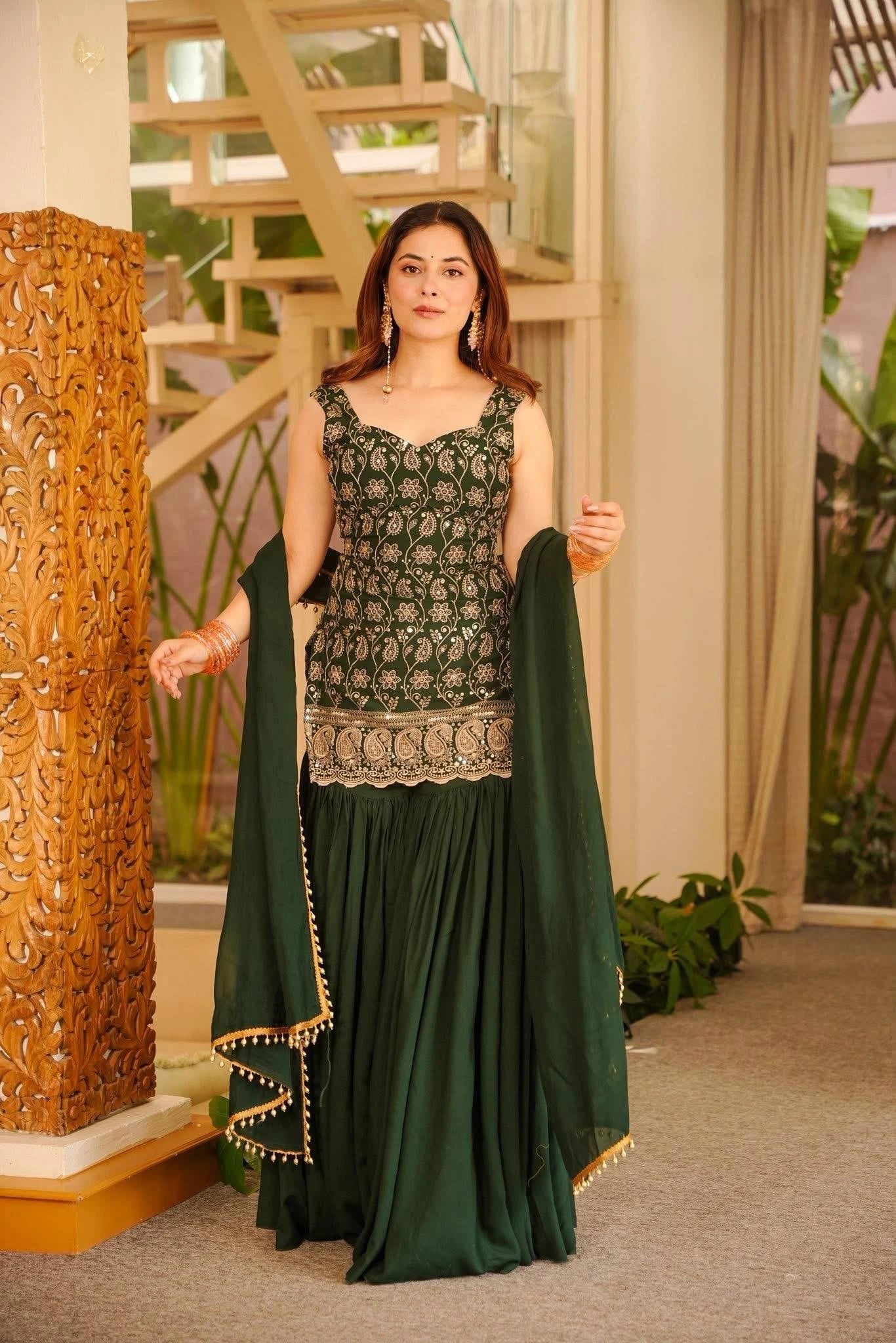 Woman in a green traditional outfit standing indoors with decorative elements.