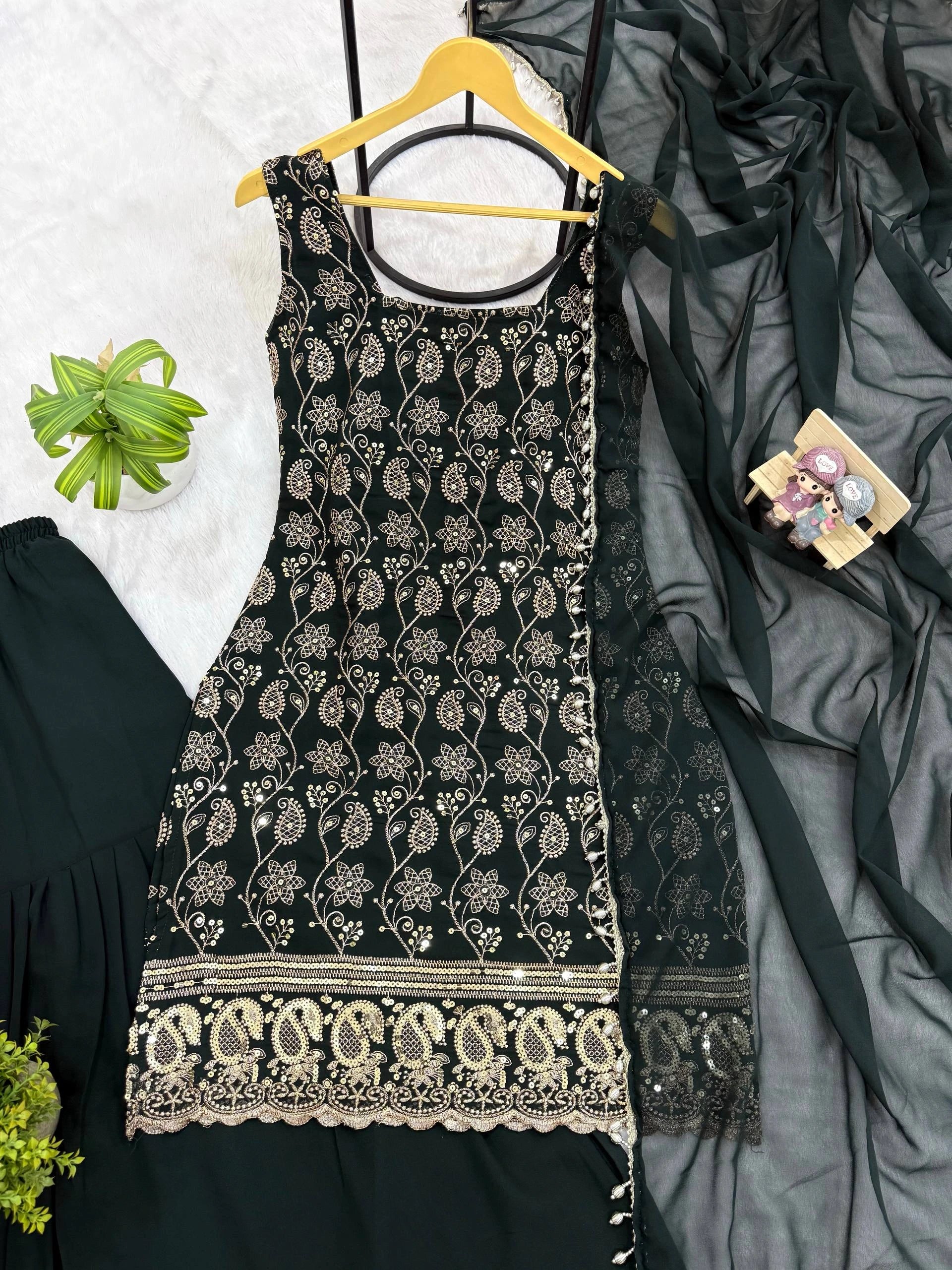 Black embroidered dress on a hanger with a gray fabric and green plant in the background