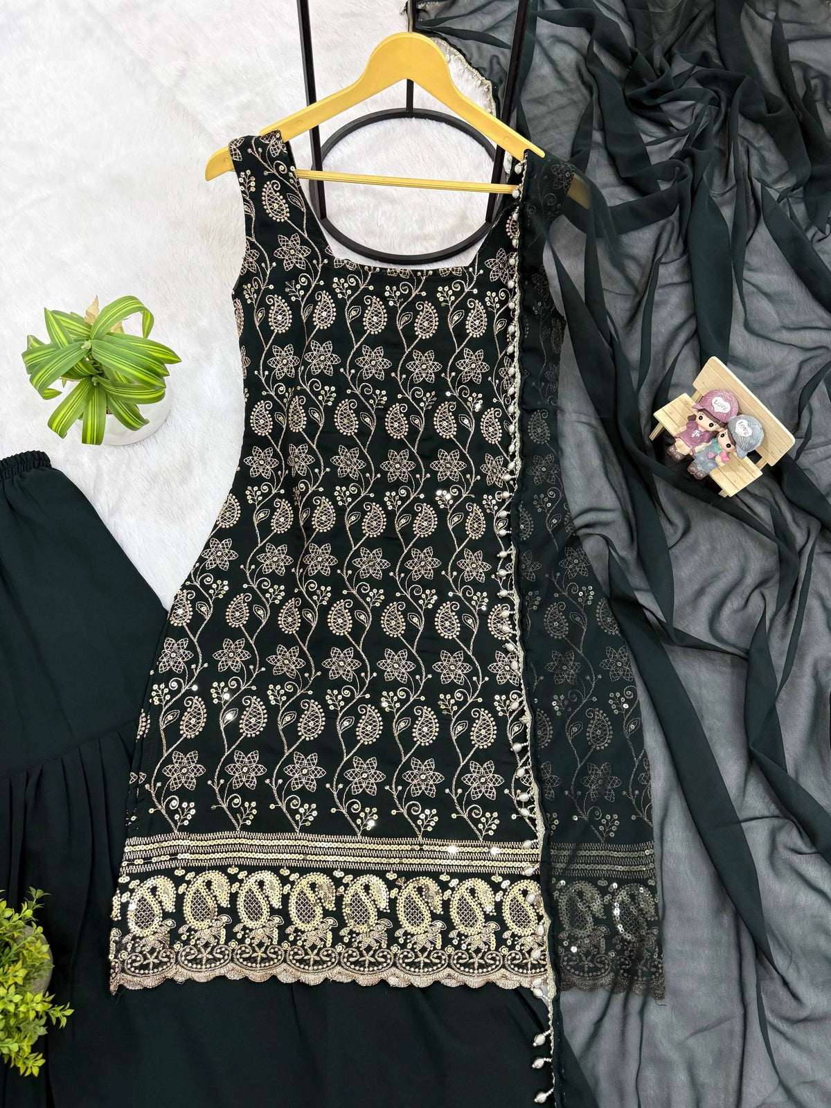 Black embroidered dress on a hanger with a gray fabric and green plant in the background