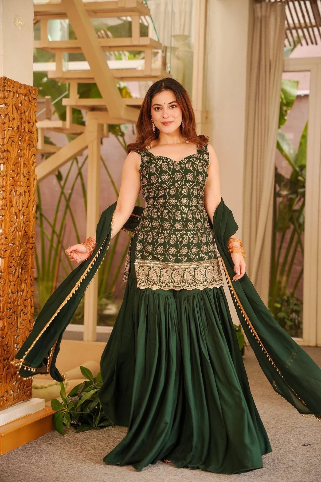 Woman in a green traditional outfit standing indoors with decorative elements.