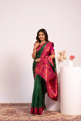 Woman in a green and pink saree standing next to a white column with flowers.