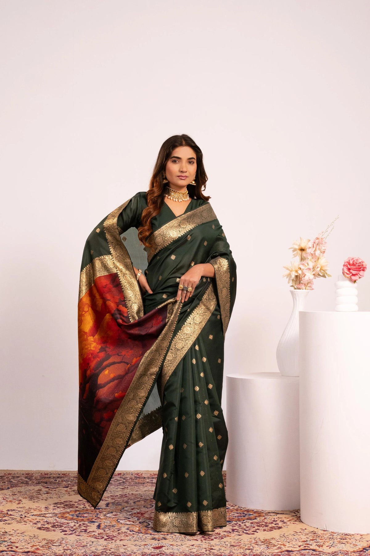 Woman wearing a dark green saree with a colorful design, standing against a white background.