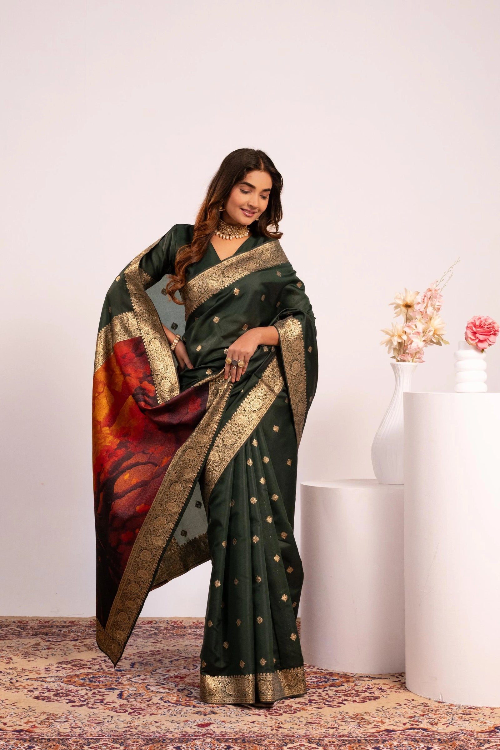 Woman wearing a dark green saree with a colorful pattern, standing against a white background.